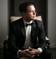 a man in a tuxedo sitting on a chair looking off to the side