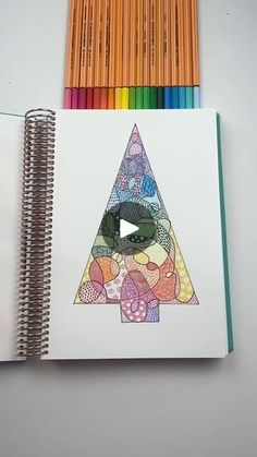 an open notebook with colored pencils next to it and a drawing on the page