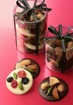 three plastic containers filled with different types of cookies and candies on top of a pink surface