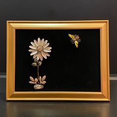 two flowers are in a gold frame on a black surface with a yellow and white butterfly