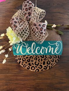 a welcome sign hanging on the side of a wooden table with flowers and burlocks