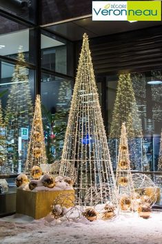 christmas trees are displayed in front of a store window with snow on the ground and behind them