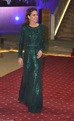 a woman in a long green dress standing on a red carpet with stairs behind her