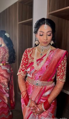 a woman in a red and pink sari standing next to another woman wearing jewelry