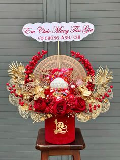 a red vase filled with flowers on top of a wooden stool next to a sign