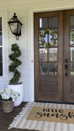 two potted plants are sitting on the front porch next to a welcome mat that says hello summer