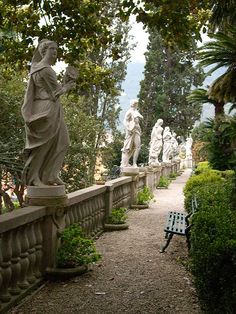 the statues are all lined up on the wall by the walkway in front of the trees