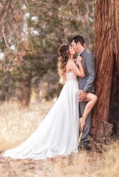 a bride and groom kissing in front of a tree at their outdoor wedding venue, surrounded by tall grass