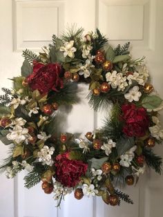 a christmas wreath with red and white flowers hanging on a front door, surrounded by greenery