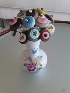 a white vase filled with lots of different colored buttons on top of a glass table