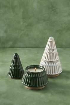 two small candles sitting next to each other on a green tablecloth covered surface, one candle is lit and the other has a cone shaped like a cone