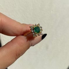 a close up of a person's hand holding a ring with an emerald and diamond center