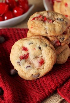 three cookies with chocolate chips and cherries on a red towel next to a bowl of cherries