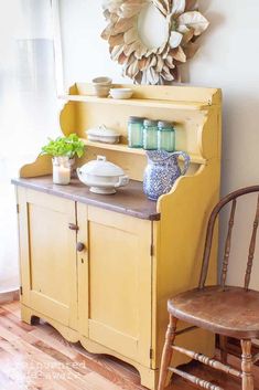 an old yellow hutch with plates and bowls on it in front of a window