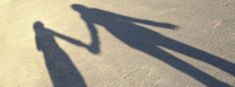 the shadow of two people holding hands on a skateboard in an empty parking lot