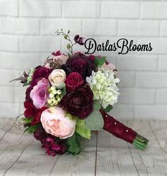 a bridal bouquet with purple and red flowers on a wooden table in front of a brick wall