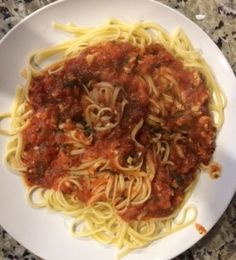 a white plate topped with pasta covered in marinara sauce on top of a marble counter