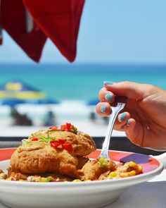 a person eating food on a plate with a beach in the backgrouf