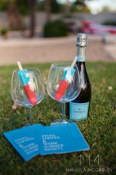 two wine glasses with toothbrushes in them sitting on the grass next to a bottle