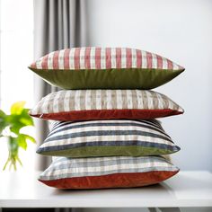 four pillows stacked on top of each other in front of a window with a potted plant