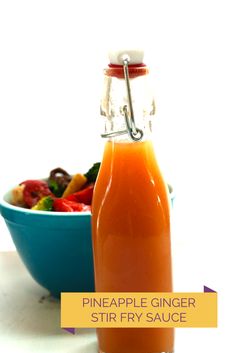 a glass bottle filled with orange liquid next to a bowl of fruit and vegetables on a table