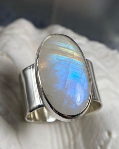 Large Rainbow Moonstone Cabochon bezel set in sterling silver on a shiny, minimalistic wide band. Ripple shoulder details accentuate this lovely oval setting. 100% handmade in Los Angeles.  Size: 9.5 Inner ring diameter: 19.6 mm Tip: Wider bands like this usually fit best a half size above your usual ring size. Compare this measurement with your favorite rings for accurate fit! Rainbow moonstone has much history and energy properties associated to it and is said to bring good fortune. See for yourself, this ring will surely bring you joy at every glance. Enjoy seeing the rainbow flash as light shines at different angles. Handmade in Los Angeles with free shipping on all US orders!  Thank you for shopping Samama Jewelry, visit my shop to see the rest of my unique jewelry designs. Discover y Modern Oval Cabochon Moonstone Ring, Modern Oval Moonstone Ring With Large Stone, Handmade Oval Moonstone Ring In Modern Style, Oval Modern Moonstone Ring With Bezel Setting, Modern Handmade Oval Moonstone Ring, Modern Moonstone Ring With Oval Bezel Setting, Modern Oval Moonstone Ring With Bezel Setting, Handmade Modern Oval Moonstone Ring, Modern Moonstone Ring With Oval Cabochon