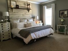 a bedroom with a bed, dressers and windows in the corner is decorated in neutral colors