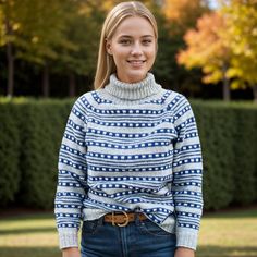 a woman wearing a blue and white sweater standing in front of a hedge with her hands in her pockets