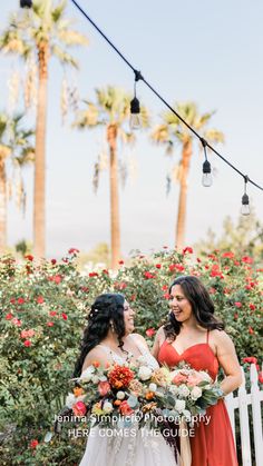 two women standing next to each other in front of trees and flowers with lights strung above them