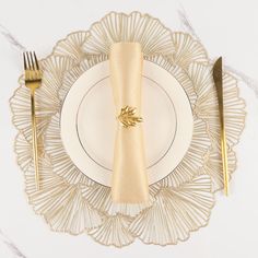 a white plate topped with a gold napkin next to a golden fork and knife set on top of it