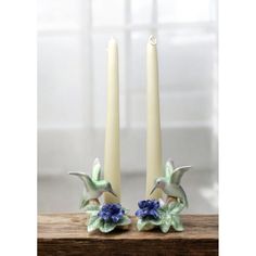 two candles sitting on top of a wooden table with blue flowers in front of them