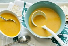 two bowls of soup with spoons and crackers on a tablecloth next to each other