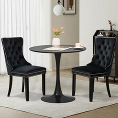 two black chairs and a round table in a room with white rugs on the floor