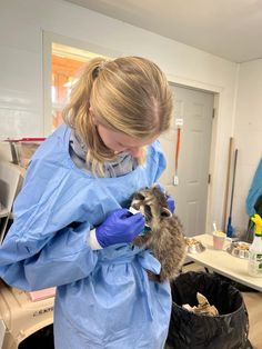 a woman in blue gown holding a baby raccoon