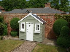 a small green shed sitting in the middle of a yard next to a brick building