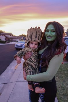 a woman holding a small child wearing a costume on the side of a road at sunset