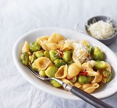 a white plate topped with pasta and vegetables next to a bowl of grated cheese