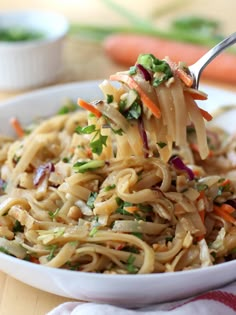 a fork full of noodles with carrots and parsley on the side in a white bowl