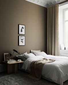 a bed sitting in a bedroom next to a window with two pictures on the wall