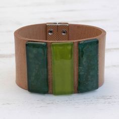 Evoking the forest three pieces of fused glass display green hues in this wristband bracelet from Brazil. Artisan duo Silvana and Joao Alexandre create this bracelet circling the wrist with a band of brown leather. Wearable Art Green Bangle Jewelry, Adjustable Recycled Glass Bracelets As Gift, Rectangular Green Bracelets As Gifts, Green Rectangular Bracelets As Gifts, Green Bangle Bracelet Wearable Art, Green Bangle Bracelet In Wearable Art Style, Handmade Wearable Art Green Bracelets, Modern Green Cuff Bracelet Gift, Handmade Green Wearable Art Bracelet