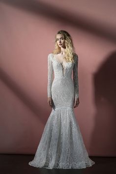 a woman in a long sleeved wedding dress standing against a pink wall with her hands on her hips