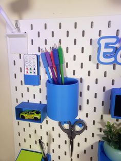 there is a blue cup with scissors and pens in it on the wall next to a toy car