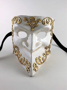 This Venetian bauta mask is handcrafted in Venice, Italy from traditional paper mache.   The mask is painted in classic white with beautiful golden designs to highlight the mask. The mask's dimensions are approximately 6" wide, 6 ¼" high and 6" deep.  The mask is handmade in Venice, Italy from paper mache and comes with certificate of authenticity. All masks are handmade in Venice, Italy. No two masks are ever identical. White And Gold Mask, White Venetian Masquerade Mask, White Venetian Mask, White Venetian Masks For Festivals, Bauta Mask, White Venetian Full-face Mask, Golden Design, Costume Masks, Costume Mask