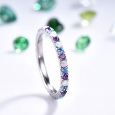 a white gold ring with multicolored stones in the middle and scattered diamonds around it