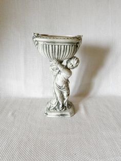 a small white vase with a baby holding it's head on the base, against a white background