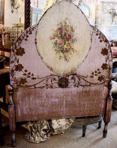 an old bed frame with flowers painted on the top and bottom, sitting in a room full of antique furniture