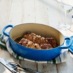 a blue pot filled with meat sitting on top of a table next to utensils