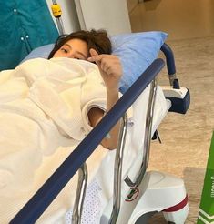 a woman laying in a hospital bed with her hand up to her face and looking at the camera