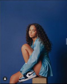 a woman sitting on top of a wooden block in front of a blue wall with her legs crossed