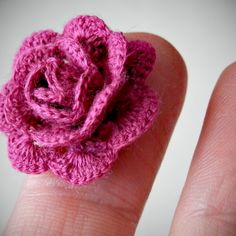 a crocheted pink flower sitting on top of a persons finger